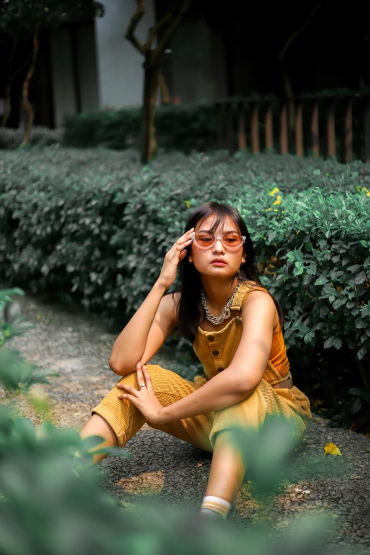 a woman sitting on the ground talking on a cell phone, a picture, inspired by Ruth Jên, trending on pexels, realism, yellow overall, lush greenery, asian girl, with sunglass