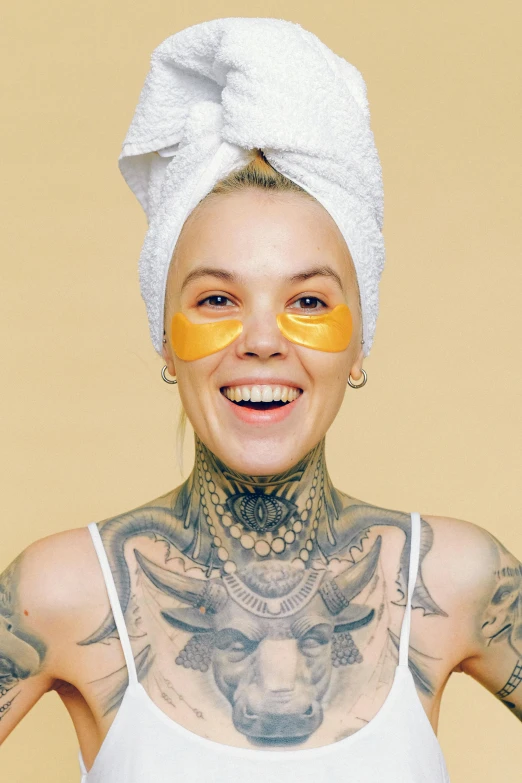 a woman with tattoos and a towel on her head, golden skin tone, smiling into the camera, with facial tattoo, uploaded