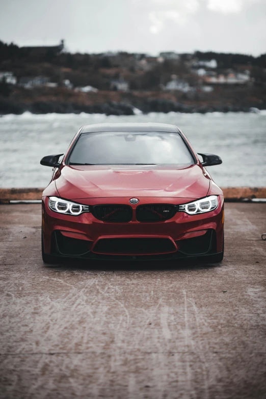 a red car parked in front of a body of water, by Adam Marczyński, pexels contest winner, renaissance, bmw, full face frontal centered, custom headlights, plain background