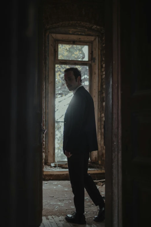 a man in a suit standing in front of a window, an album cover, unsplash, in a derelict house, denis villeneuve cinematography, about to enter doorframe, ((portrait))