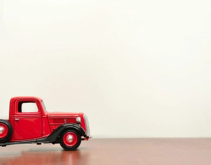 a red toy truck sitting on top of a wooden table, pexels contest winner, photorealism, vintage cars, with a white background, 1 9 3 7, minimalist composition