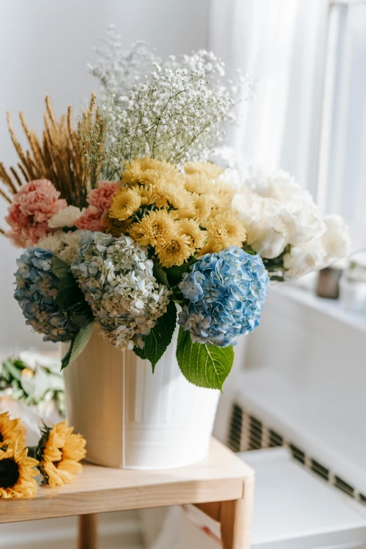 a vase filled with flowers sitting on top of a wooden table, light grey blue and golden, hydrangea, multi chromatic, embracing