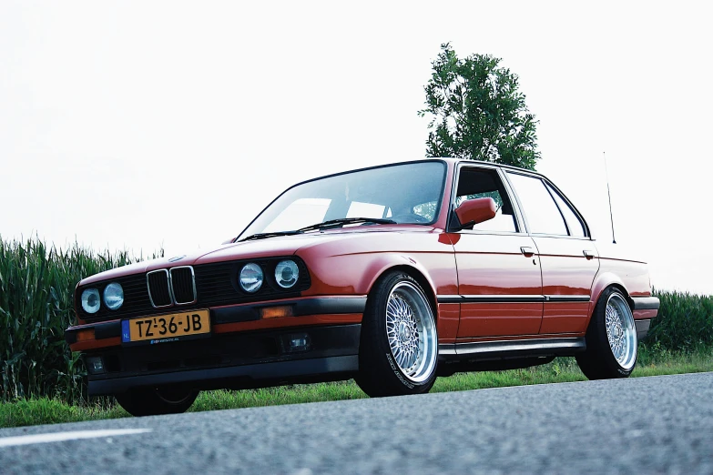 a red car is parked on the side of the road, a picture, by Jan Tengnagel, unsplash, renaissance, bmw e 3 0, brown red blue, medium format. soft light, 3 ds max + v - ray