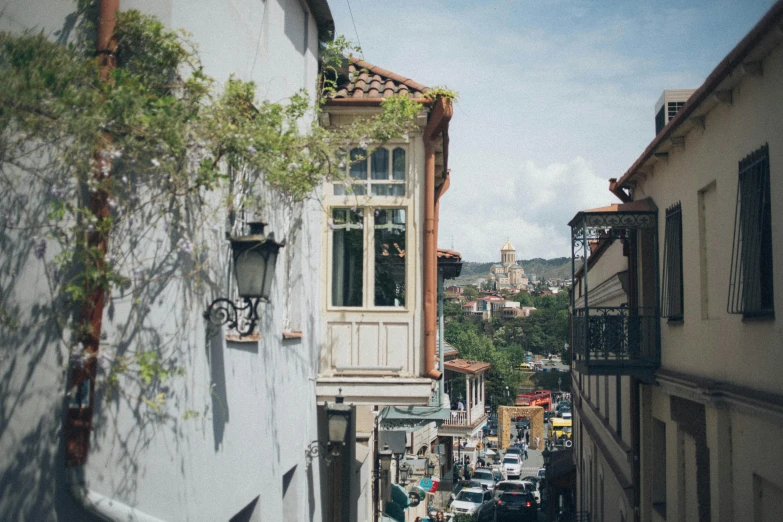 a street filled with lots of traffic next to tall buildings, inspired by Ceferí Olivé, pexels contest winner, quito school, house on a hill, ivory and copper, colonial style, facing away