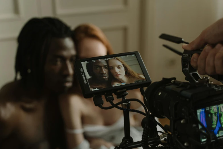 a close up of a person holding a camera, two models in the frame, man is with black skin, tv production, everything fits on the screen