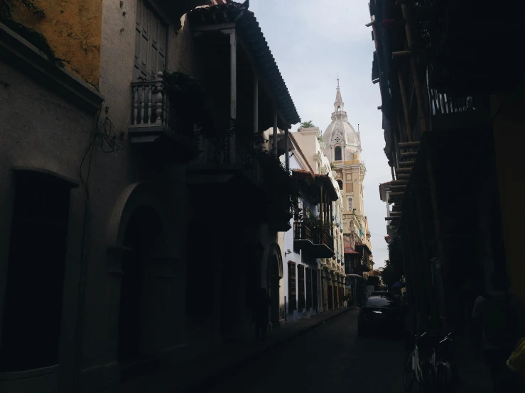 a narrow street with a clock tower in the background, pexels contest winner, baroque, colombian, beige and dark atmosphere, from afar, leaked image