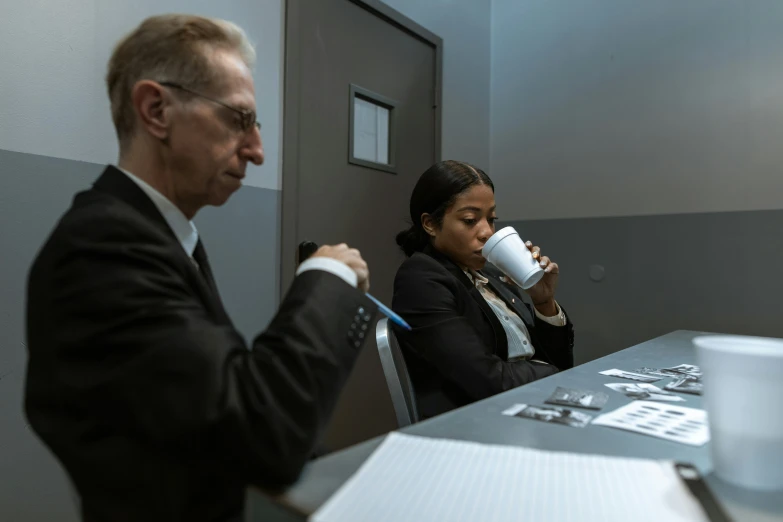 two people sitting at a table with a cup of coffee, a photo, by Matthias Stom, private press, secret service photos, in a research facility, from marvel studios, alexandria ocasio - cortez