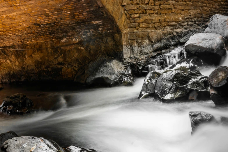 a small waterfall flowing under a stone bridge, by Daniel Seghers, pexels contest winner, snow cave, thumbnail, multiple stories, metal towers and sewers