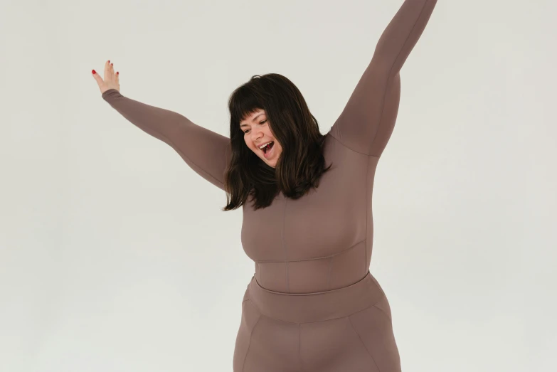 a woman with her arms in the air, by Nyuju Stumpy Brown, silicone skin, peter griffin body type, wearing a tracksuit, muted brown