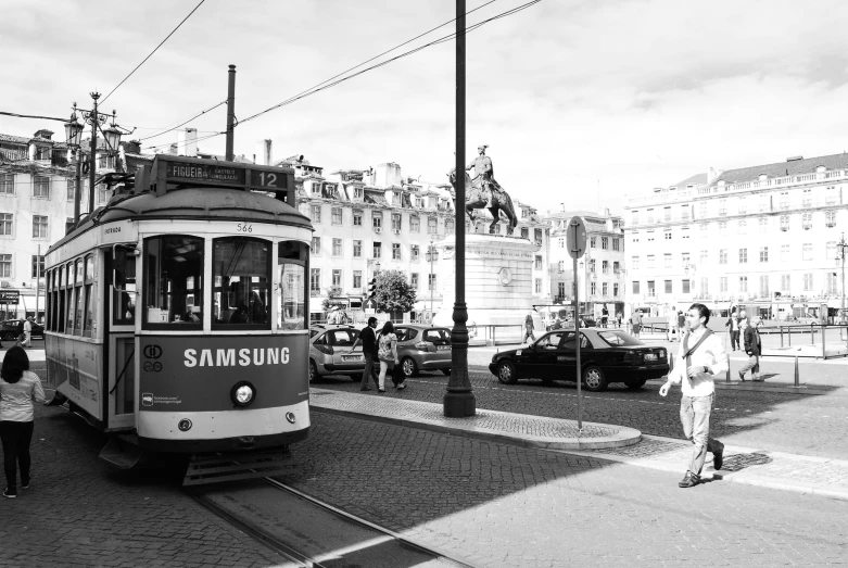 a black and white photo of a trolley on a city street, by Emma Andijewska, pexels contest winner, art nouveau, helsinki, square, sunny sky, people