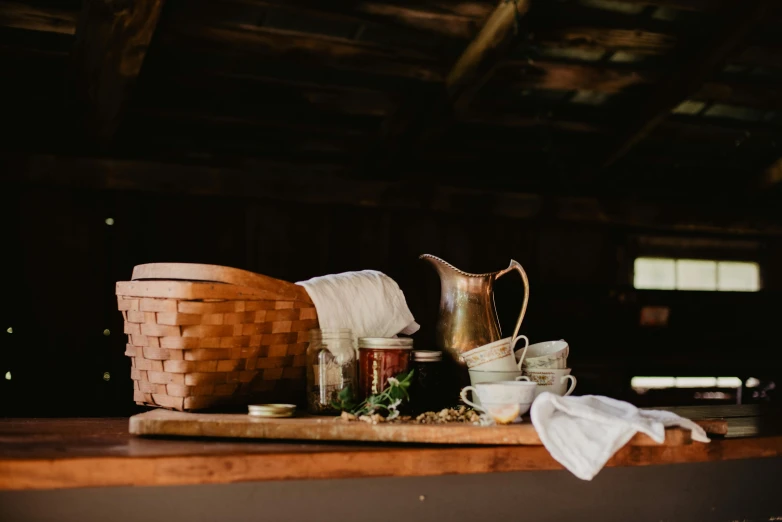 a basket sitting on top of a wooden table, a still life, by Jessie Algie, unsplash, pilgrim village setting, ingredients on the table, inside a barn, wood cups