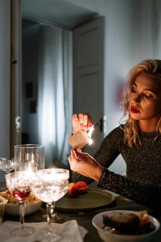 a woman sitting at a table with a candle in her hand, trending on pexels, with sparking circuits, blonde swedish woman, family dinner, emitting light ornaments