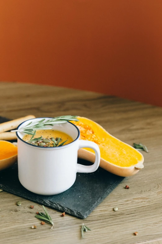 a cup of soup sitting on top of a wooden table, a still life, unsplash, pumpkin, multiple stories, high resolution photo, slate