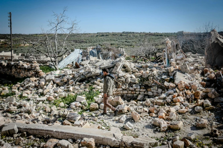 a man standing in front of a pile of rubble, by Nathalie Rattner, unsplash, les nabis, al - qadim, seen from far away, makeshift house, walking towards the camera