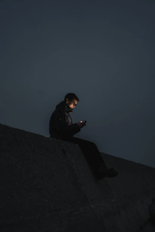 a man sitting on a wall looking at his cell phone, trending on pexels, minimalism, dark sky, 6 : 3 0 am, gaming, dark. no text