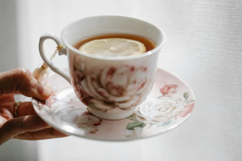 a close up of a person holding a cup of tea, by Lucia Peka, pexels, rococo, lemon, rose twining, round-cropped, made of glazed