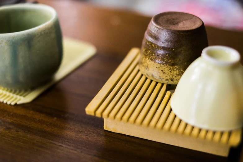 a couple of cups sitting on top of a wooden table, inspired by Kanō Shōsenin, trending on unsplash, mingei, square, yellow, carrying a tray, unedited