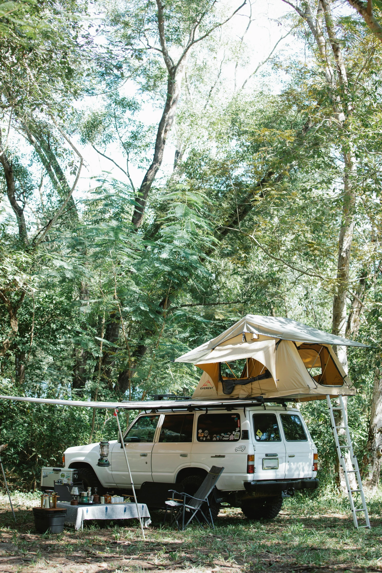 a van parked in the woods with a tent on top of it, madagascar, soft top roof raised, sunny day time, square