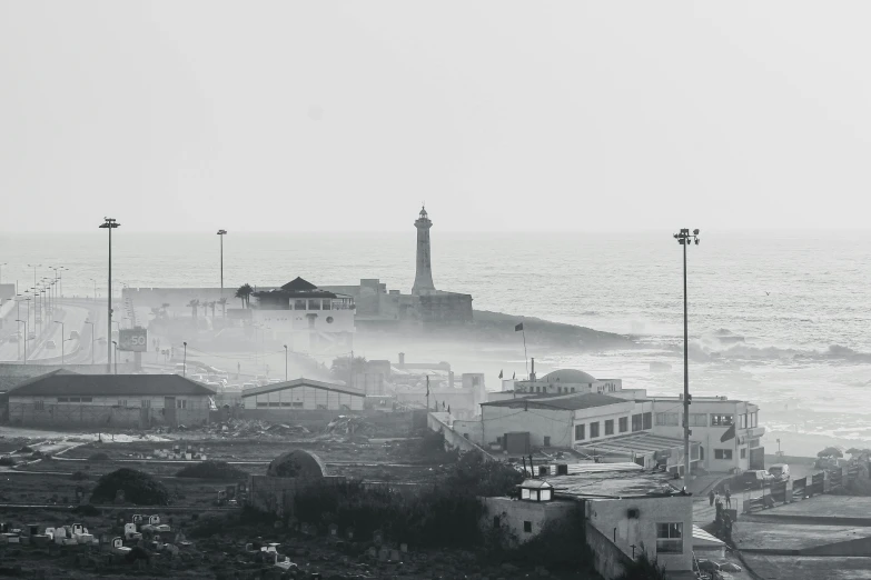 a black and white photo of a city by the ocean, by David Begbie, pexels contest winner, light haze, moroccan city, lighthouse, burned city