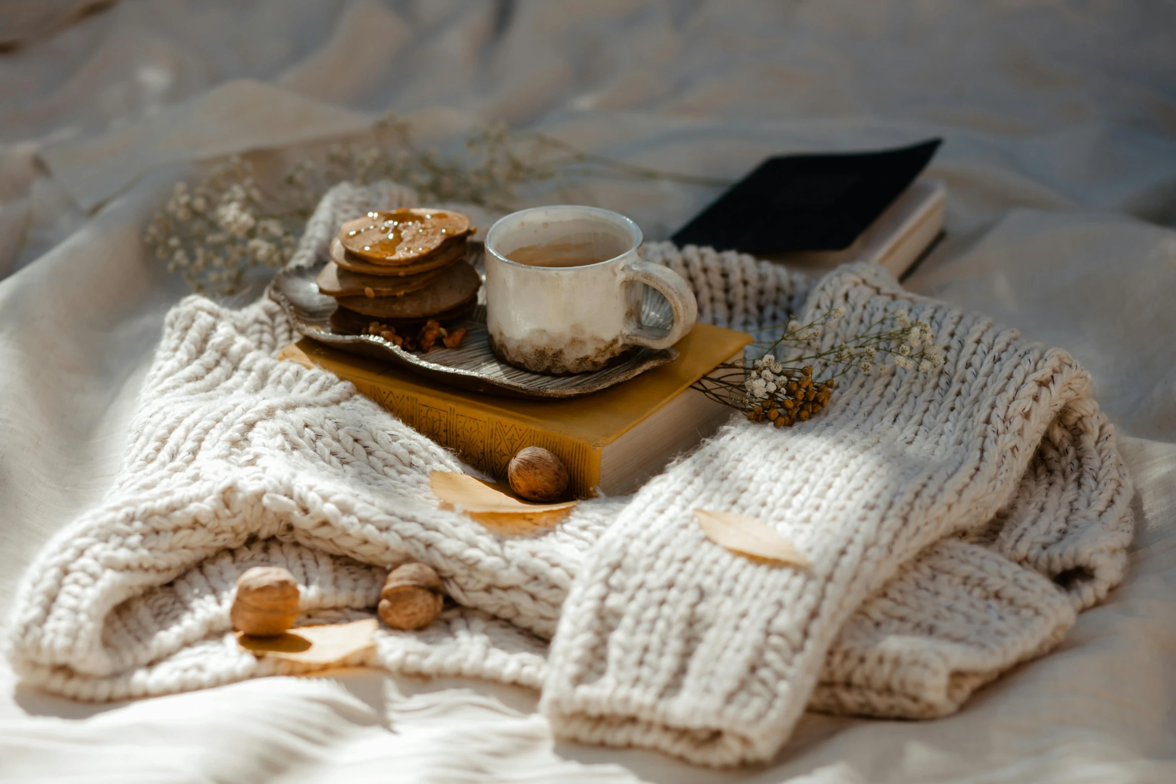 a blanket sitting on top of a bed next to a cup of coffee, a still life, trending on pexels, romanticism, brown sweater, snacks, storybook style, piled around