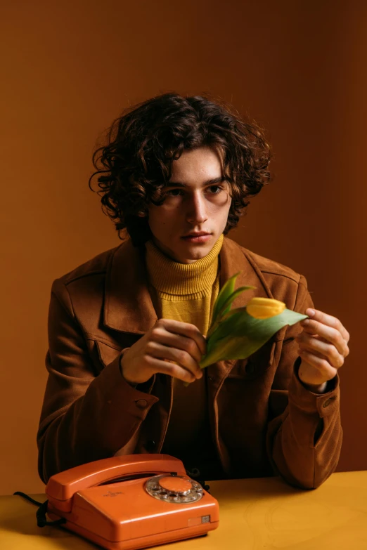 a man sitting at a table in front of a phone, an album cover, inspired by Luca Zontini, trending on pexels, sitting on a leaf, elegant yellow skin, brown curly hair, model shoot