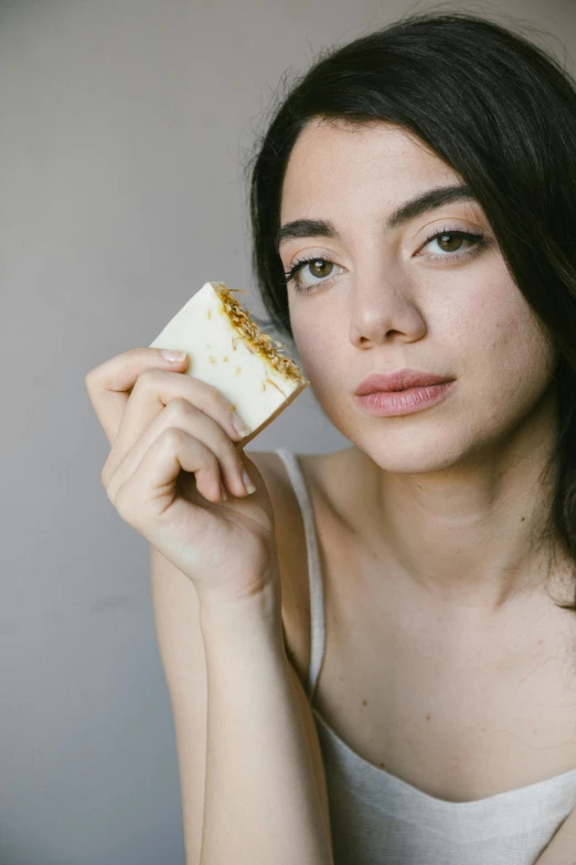 a woman holding a piece of food in her hand, a portrait, by Jessie Algie, unsplash, carved soap, white and gold, square, aubrey plaza