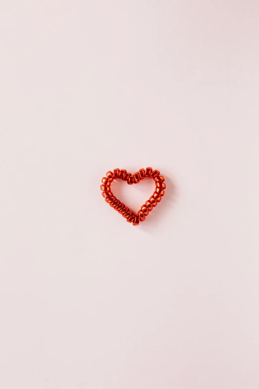 a red beaded heart on a white surface, trending on pexels, made of wire, pink, design, item