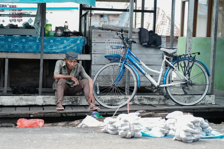 a man sitting on a bench next to a bike, pexels contest winner, sumatraism, plastic waste, bags on ground, fish seafood markets, a friend in need