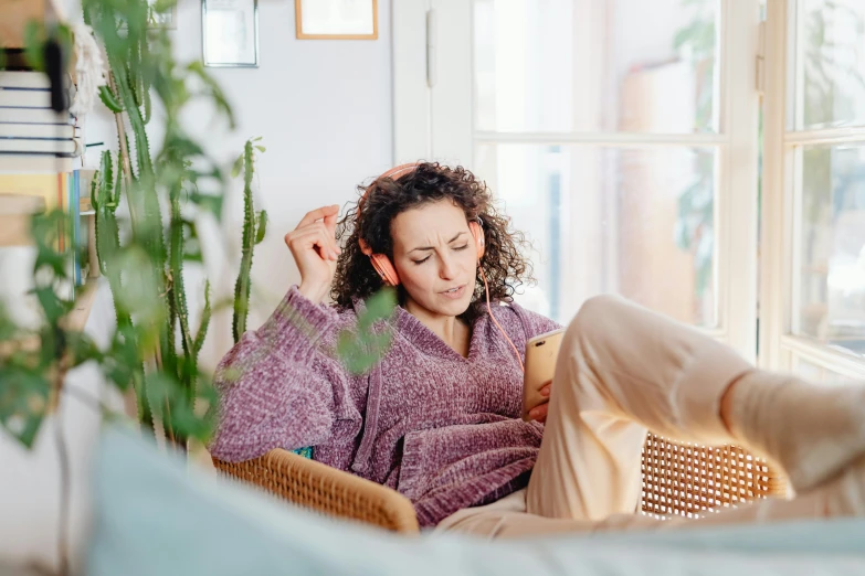 a woman sitting on a couch in a living room, trending on pexels, wearing purple headphones, trying to read, curly haired, ewa juszkiewicz