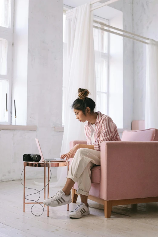 a woman sitting on a pink couch using a laptop, trending on pexels, sitting in an empty white room, gif, multiple stories, asian woman