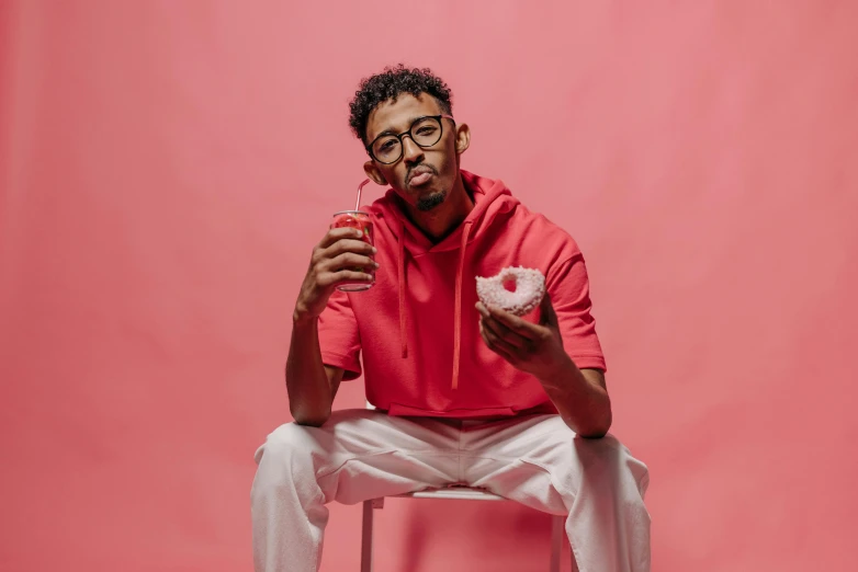 a man sitting on a chair eating a donut, an album cover, inspired by Justin Sweet, pexels contest winner, antipodeans, pink clothes, mkbhd, man with glasses, casual pose