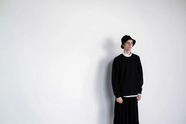 a man standing in front of a white wall, a character portrait, inspired by Shōzaburō Watanabe, unsplash, purism, wearing a black sweater, nun fashion model, 15081959 21121991 01012000 4k, dezeen
