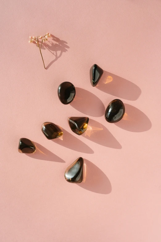 a group of earrings sitting on top of a pink surface, by Julia Pishtar, large obsidian crystals, - 9, amber, beans