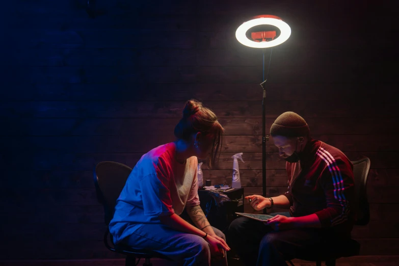 a couple of people that are sitting down, pexels contest winner, serial art, ring light, an escape room in a small, cinestill 800t eastmancolor, person in foreground