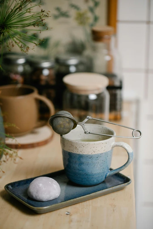 a cup of tea and a spoon on a tray, a still life, unsplash, soft grey and blue natural light, thumbnail, hut, vanilla