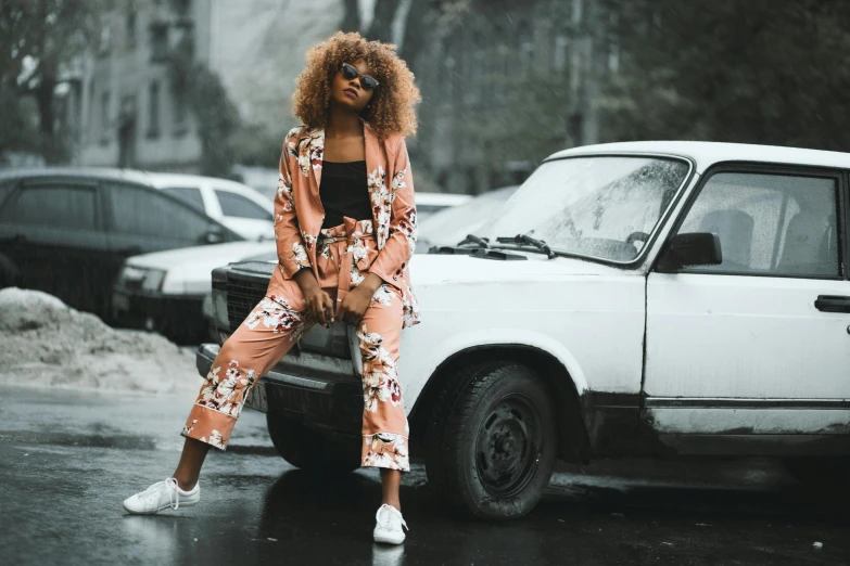 a woman sitting on a car in the rain, trending on pexels, graffiti, stylish suit, floral clothes, brown skinned, in shades of peach