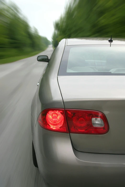 a silver car driving down a road with trees in the background, tail lights, thumbnail, average, feature