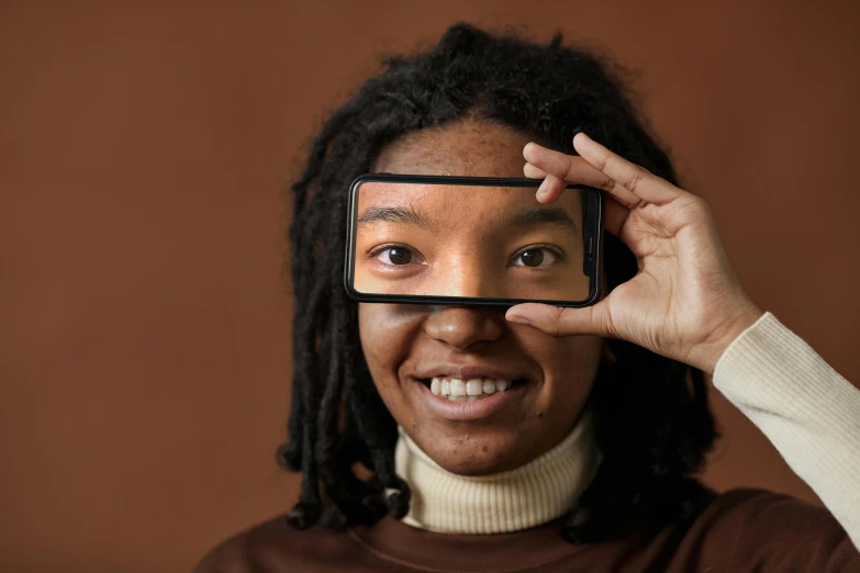 a woman holding up a cell phone to her face, trending on pexels, afrofuturism, square rimmed glasses, brown, rectangle, spherical lens