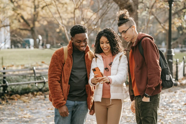 a group of people standing next to each other looking at a cell phone, trending on pexels, fall season, avatar image, student, brown