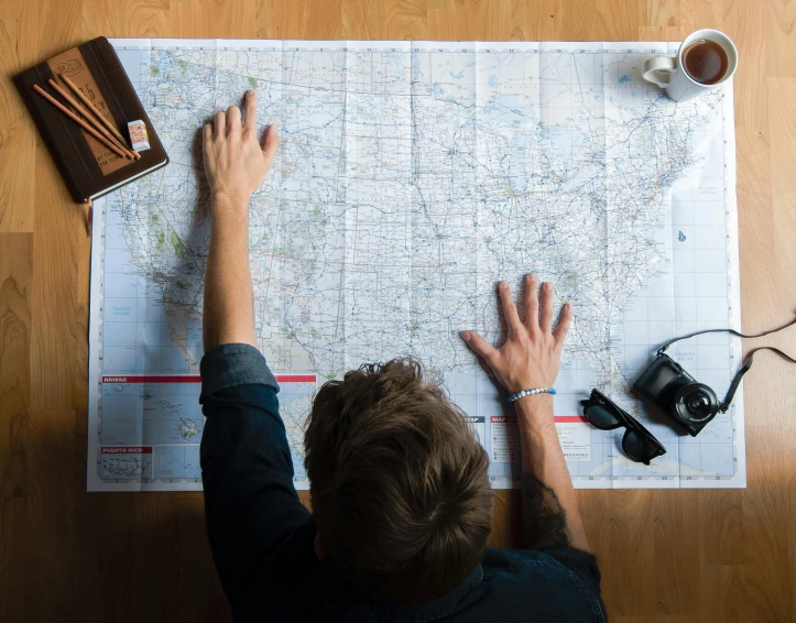 a man sitting at a table looking at a map, by Jessie Algie, trending on unsplash, aerial view from above, national geographics, instagram photo, large format