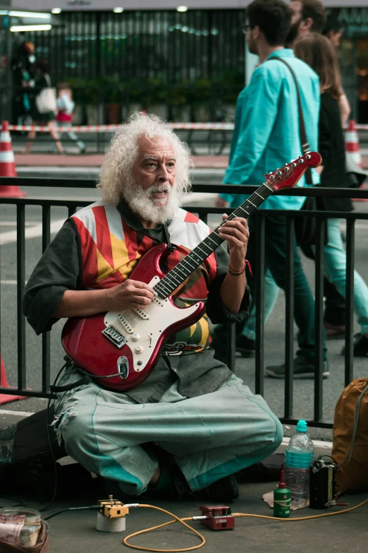 a man sitting on the ground playing a guitar, curly white hair, trending in japan, in paris, recognizable