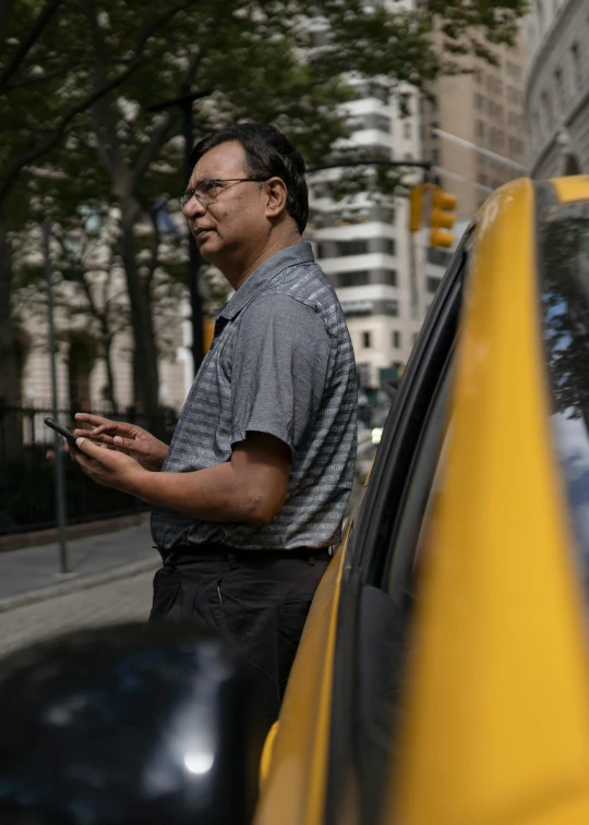 a man standing next to a yellow car on a city street, new york times, profile picture, phone photo, ap news photo