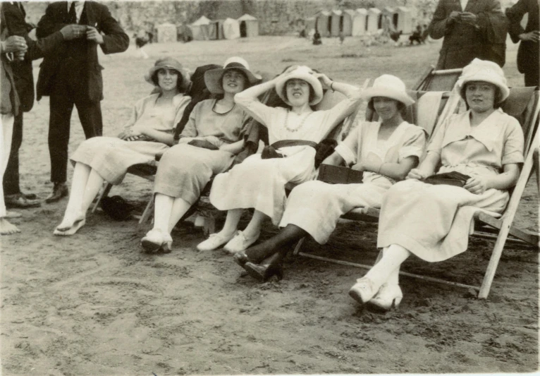 a group of women sitting on top of a wooden bench, a black and white photo, by Elsie Henderson, art nouveau, wearing a white bathing cap, spectators, in a sun lounger, 120mm black and white photograph