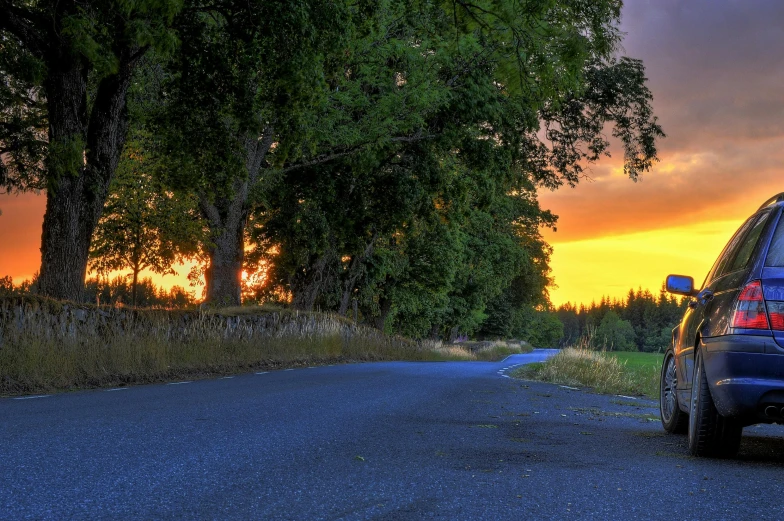 a car is parked on the side of the road, by Jessie Algie, pexels contest winner, tree-lined path at sunset, new zealand, blue and orange, sunset panorama