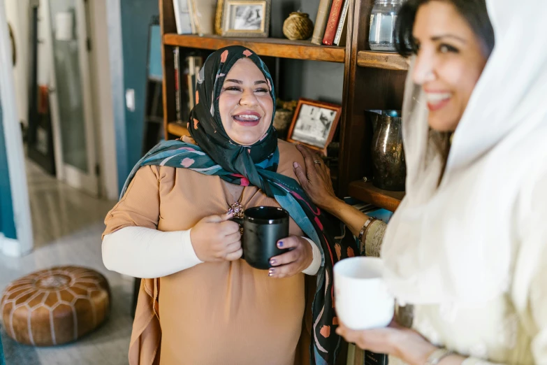 a couple of women standing next to each other, by Arabella Rankin, pexels contest winner, hurufiyya, is ((drinking a cup of tea)), mutahar laughing, full figured, middle eastern skin