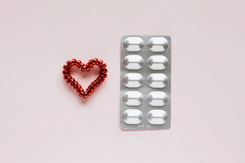 a couple of pills and a heart on a pink background, a picture, by Julia Pishtar, pexels, made out of shiny white metal, red and grey only, contracept, iron