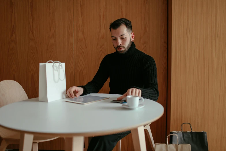 a man sitting at a table reading a magazine, by Adam Marczyński, pexels contest winner, wearing turtleneck, minimalist home office, gif, customers