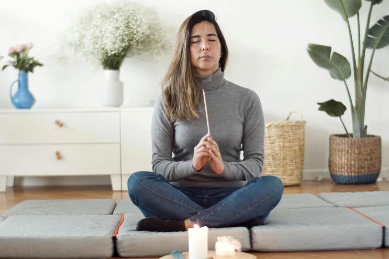 a woman sitting on a yoga mat in front of a candle, trending on pexels, holding a wooden staff, wearing a turtleneck and jacket, displayed on an altar, grey