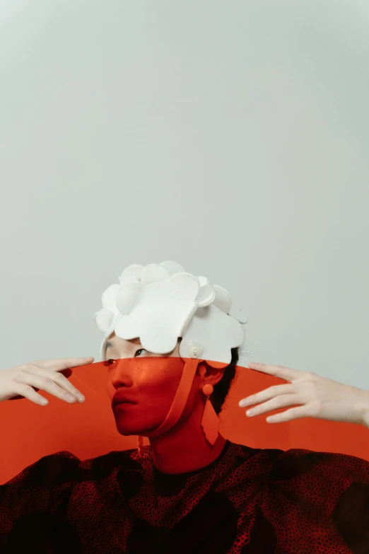 a man covering his face with a piece of paper, an album cover, by Anna Füssli, aestheticism, coral headdress, high quality photo, red and white, ignant