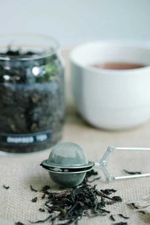 a tea strainer sitting on top of a table next to a cup of tea, unsplash, terrarium, gunmetal grey, hero shot, organic detail